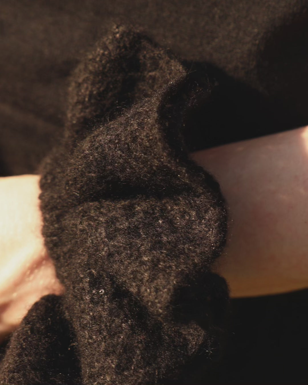 Black coloured knitted cashmere scrunchie worn on a model's wrist. 
