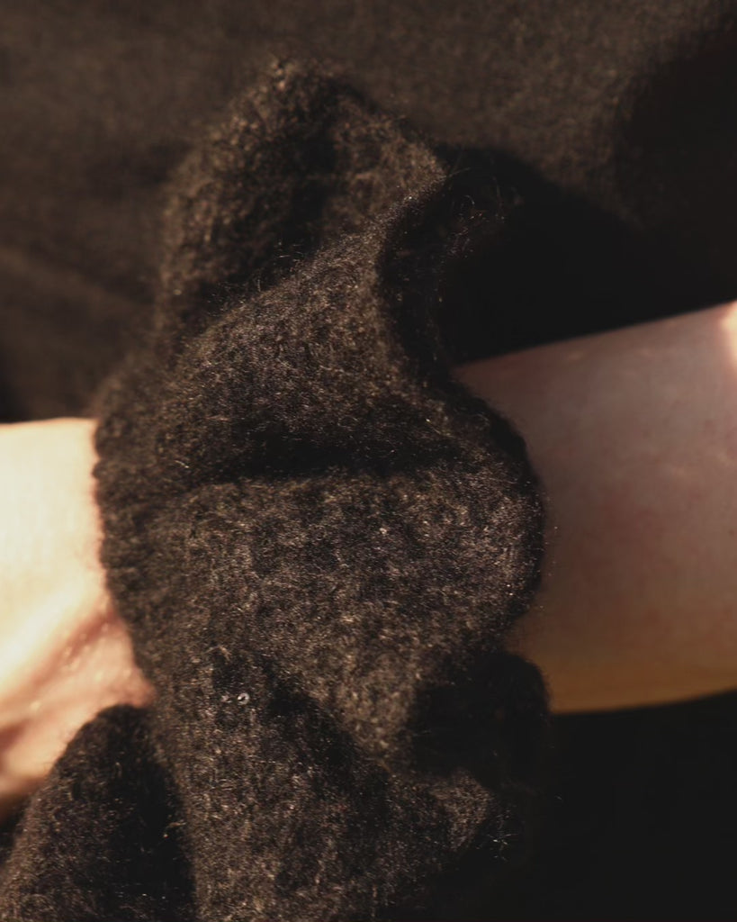 Black coloured knitted cashmere scrunchie worn on a model's wrist. 